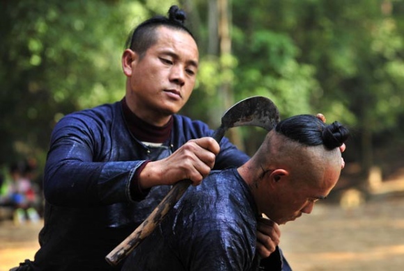 Homem usa foice para raspar cabelo de membro de aldeia