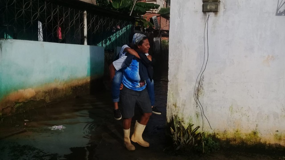 Após forte chuva, mães carregam filhos nas costas para conseguirem chegar à escola